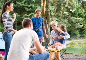A happy family enjoying time at the park, gathered around a barbecue with drinks and food.