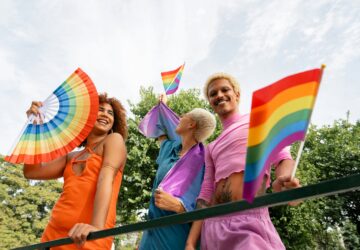A group of people standing together, holding colorful rainbow umbrellas.