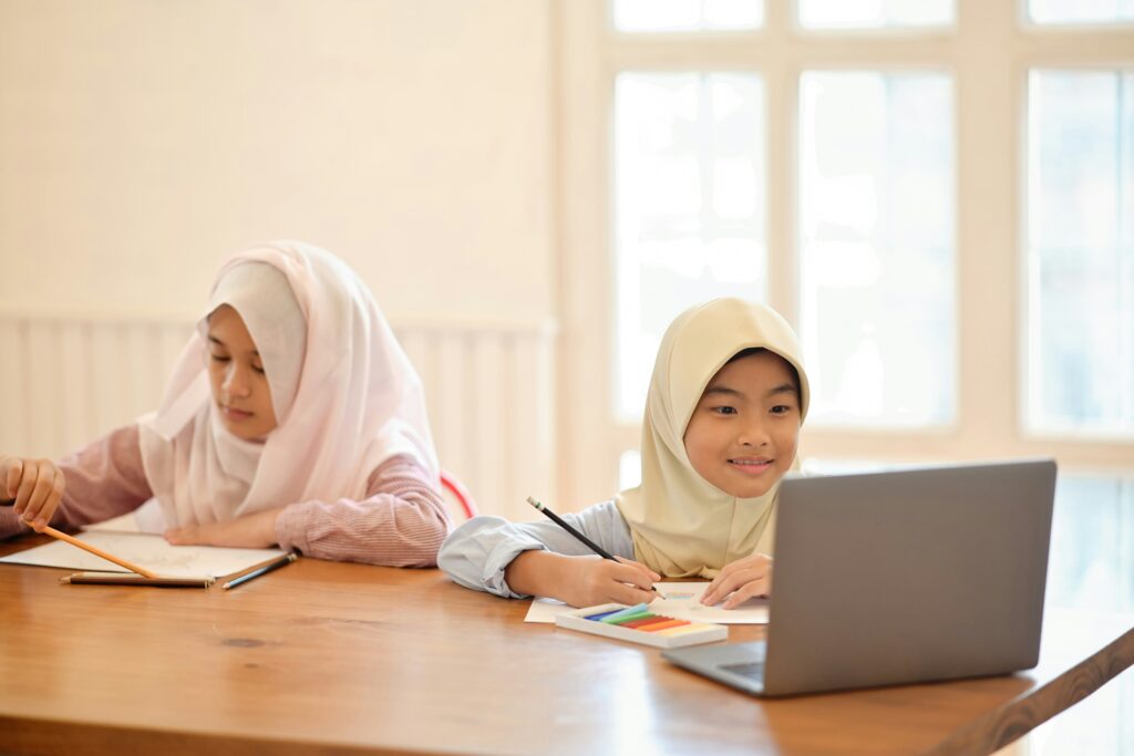 Two children focused on their computers, sitting side by side and engaging in a digital learning activity.