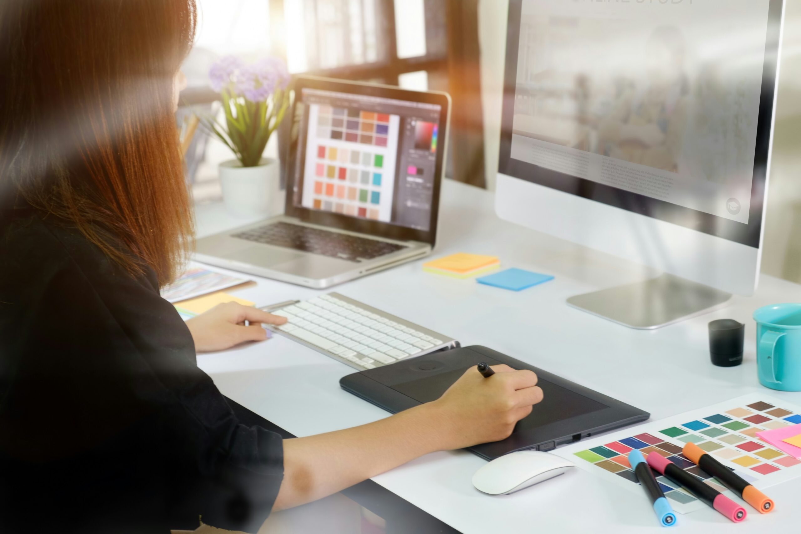 Young professional woman using a digital tablet while working on a computer in an office.
