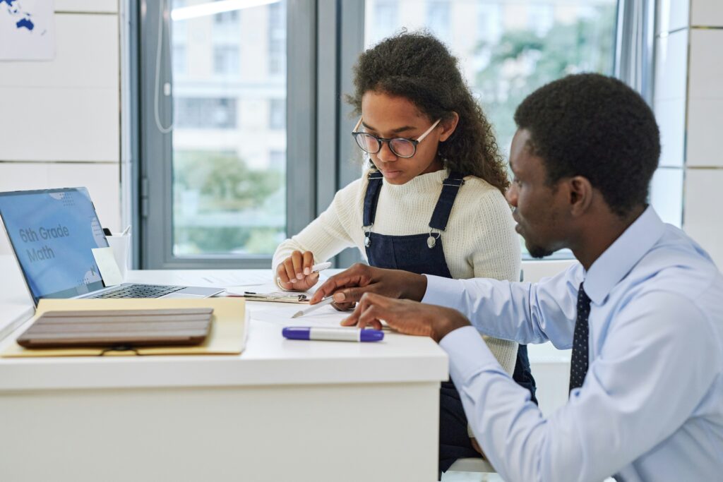 A young Black tutor helping a schoolgirl with a test, both engaged in the learning process.