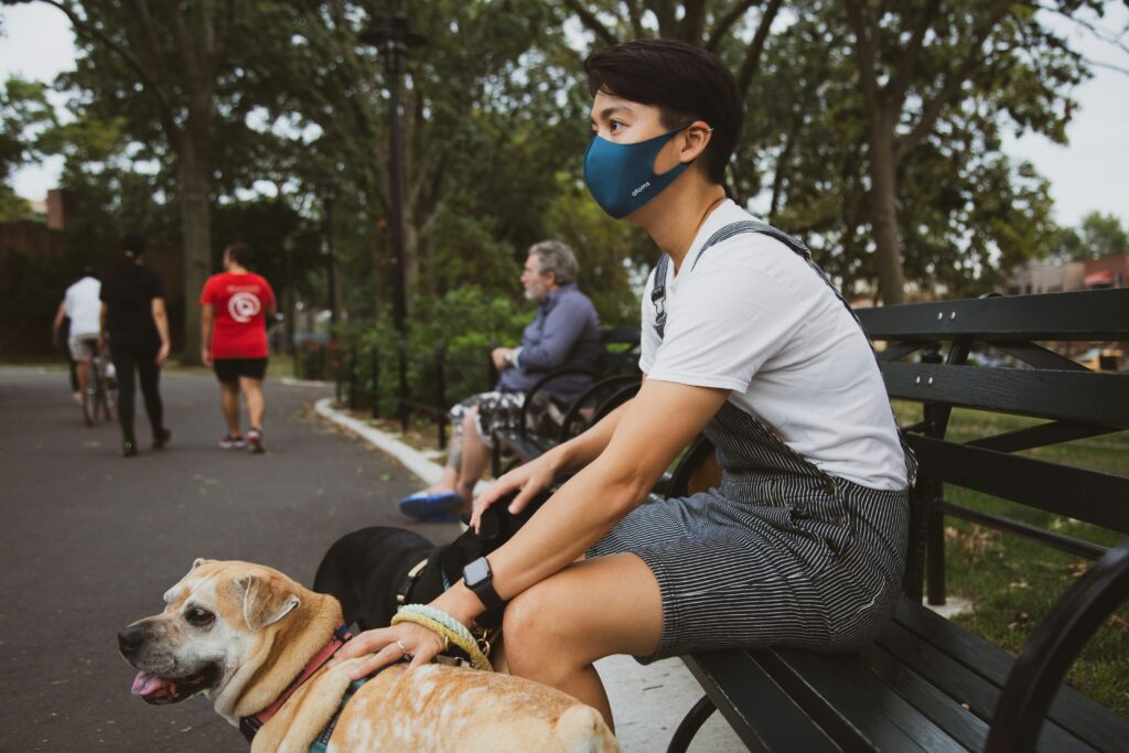 Man in a white t-shirt sitting on a bench beside a brown dog, both relaxing outdoors.