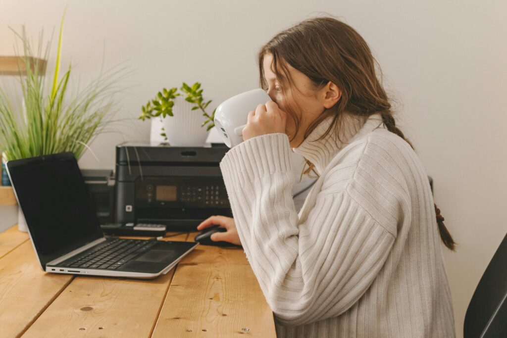 A woman sitting at a table with a laptop, focused on her work in a bright and cozy environment.