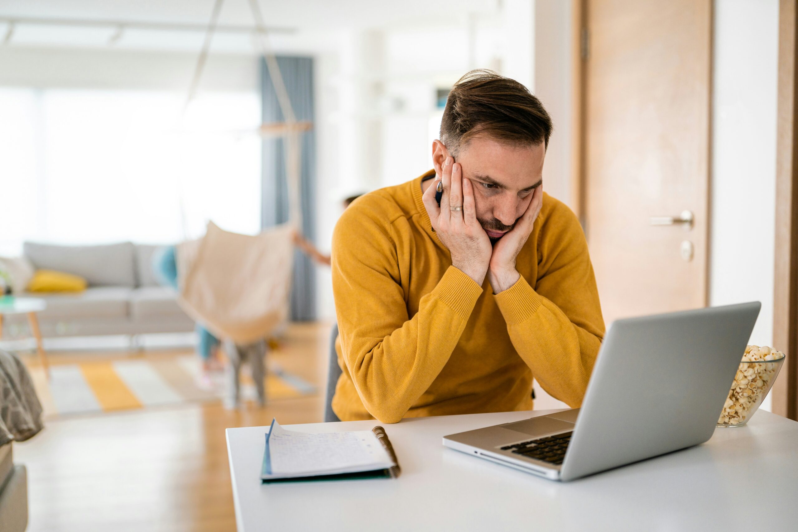 Frustrated man working on a laptop at home, looking stressed.